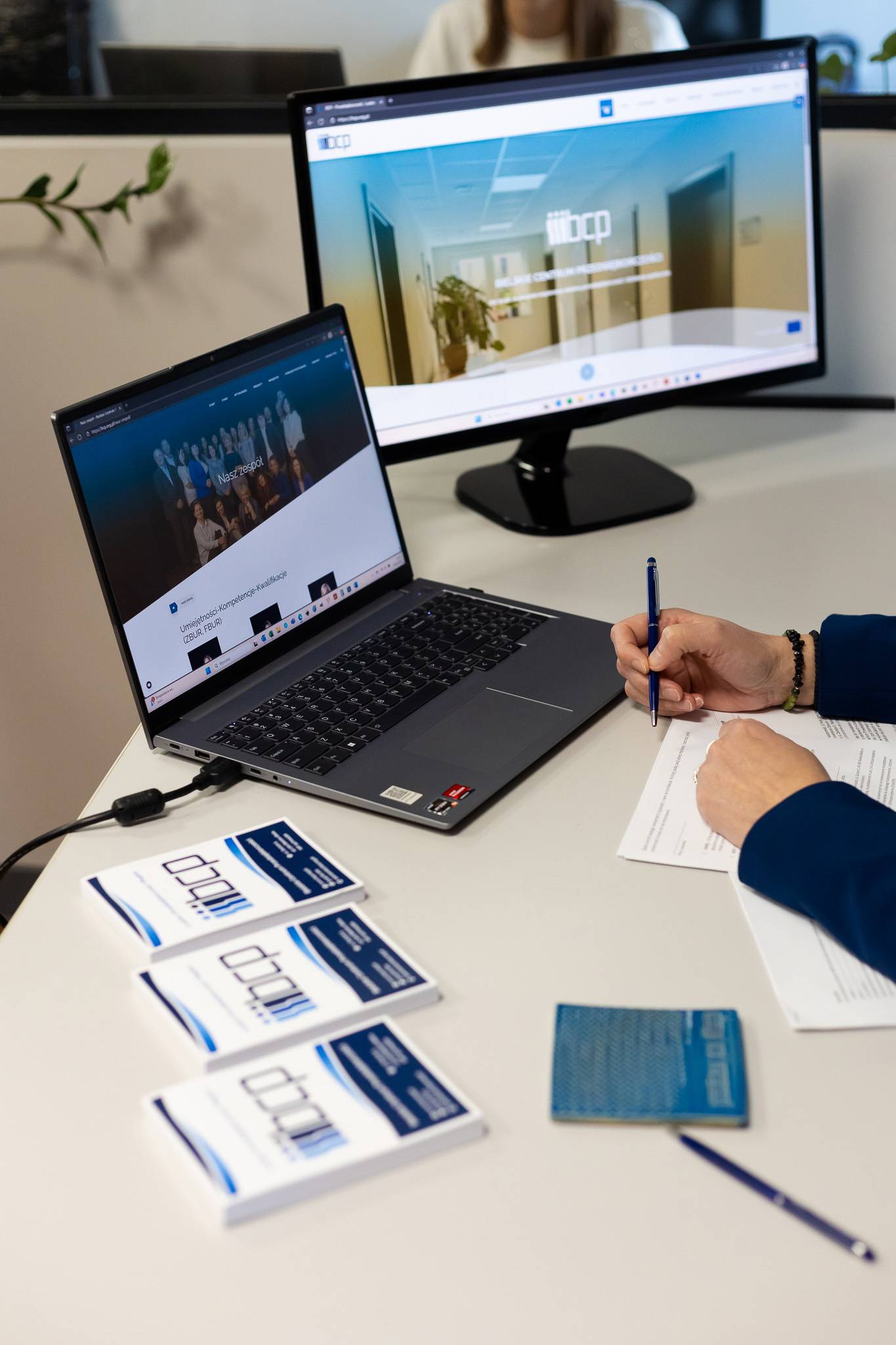 Zdjęcie przedstawia blat biurka z notesami i ręką